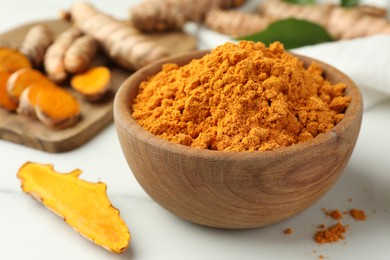 Aromatic turmeric powder and raw roots on white table, closeup