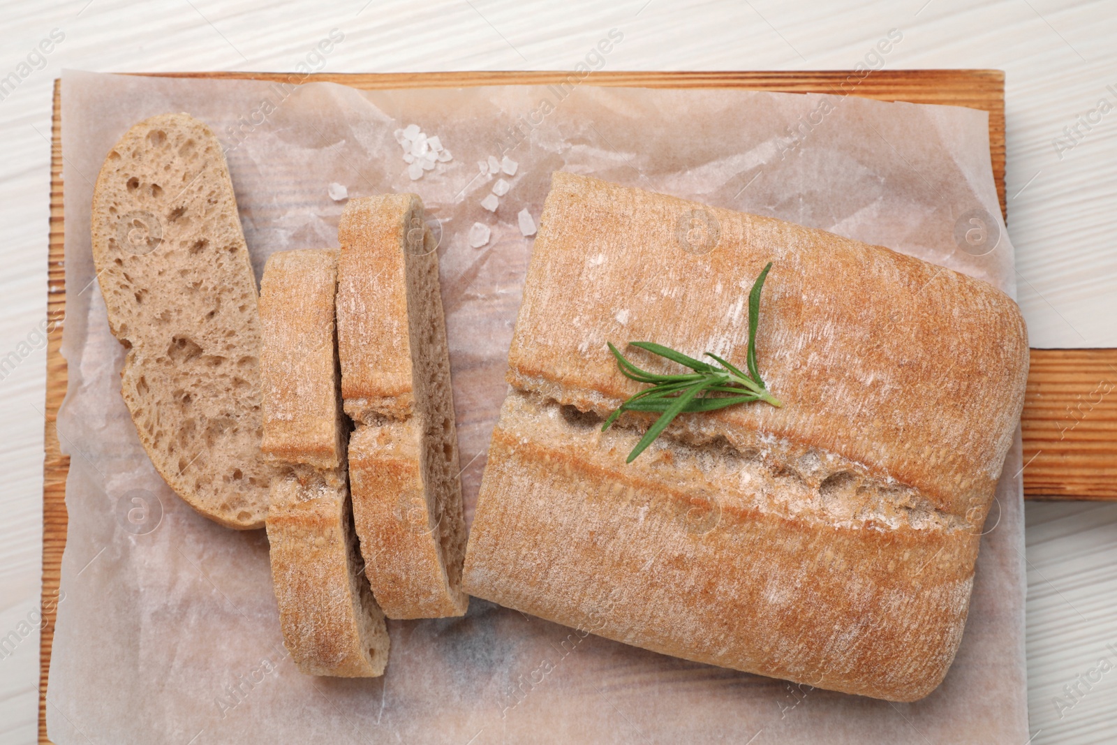 Photo of Fresh crispy ciabatta with rosemary on white wooden table, top view