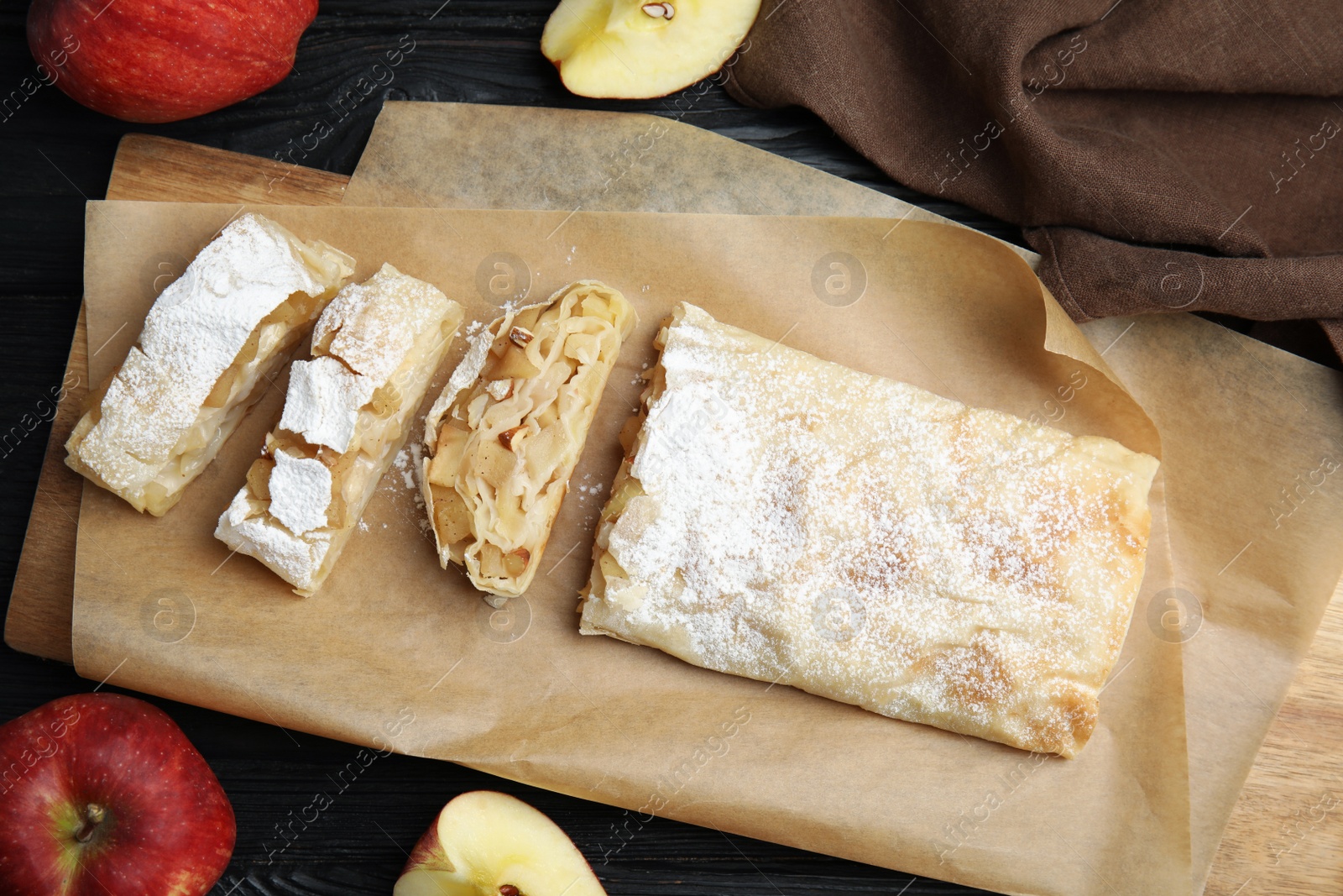 Photo of Delicious strudel and fresh apples on black wooden table, flat lay