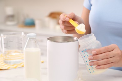 Woman preparing infant formula at table indoors, closeup. Baby milk