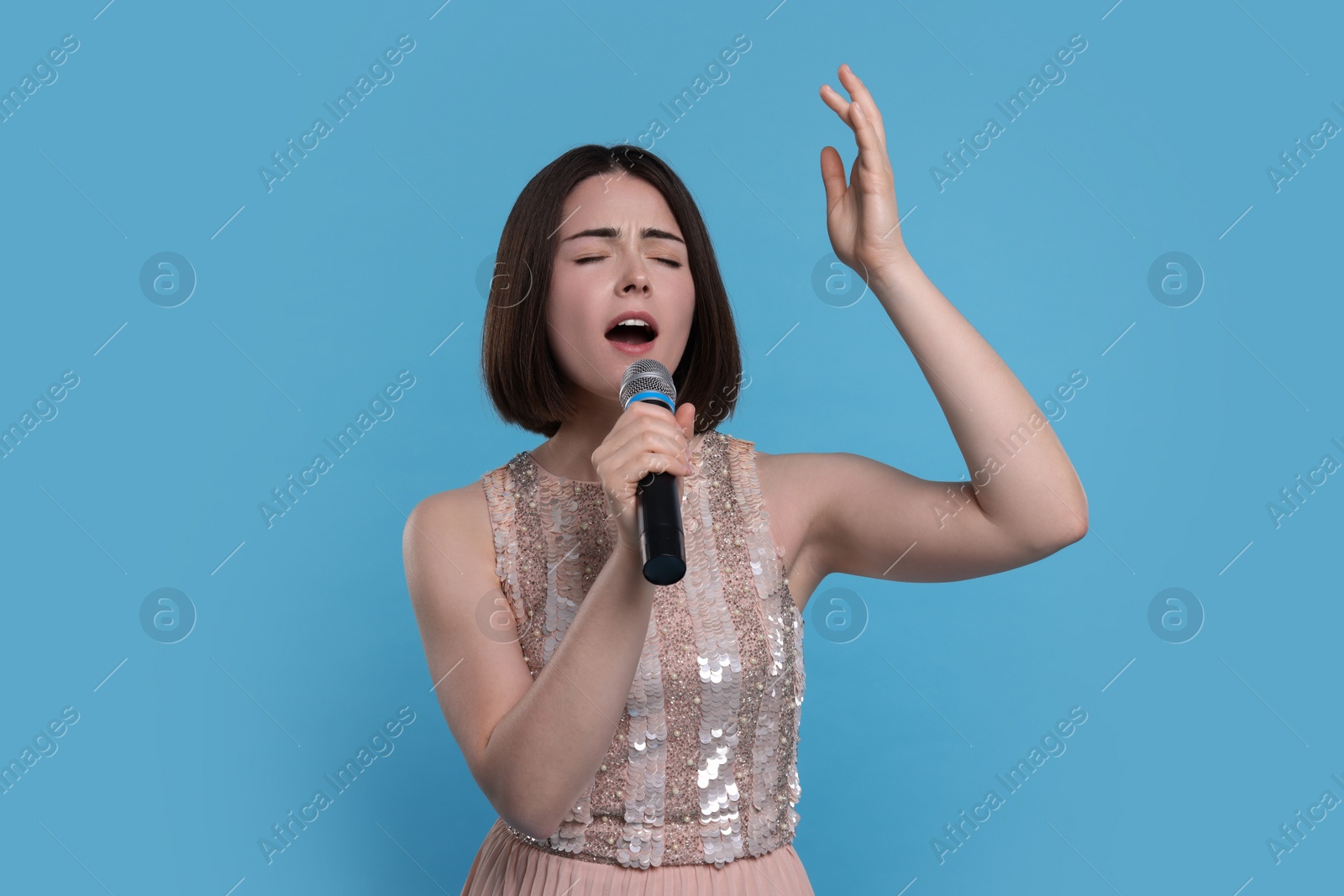 Photo of Beautiful young woman with microphone singing on light blue background