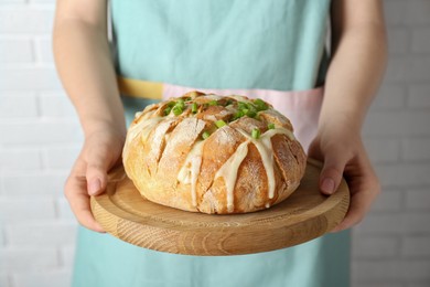Woman holding freshly baked bread with tofu cheese and green onion on light background, closeup