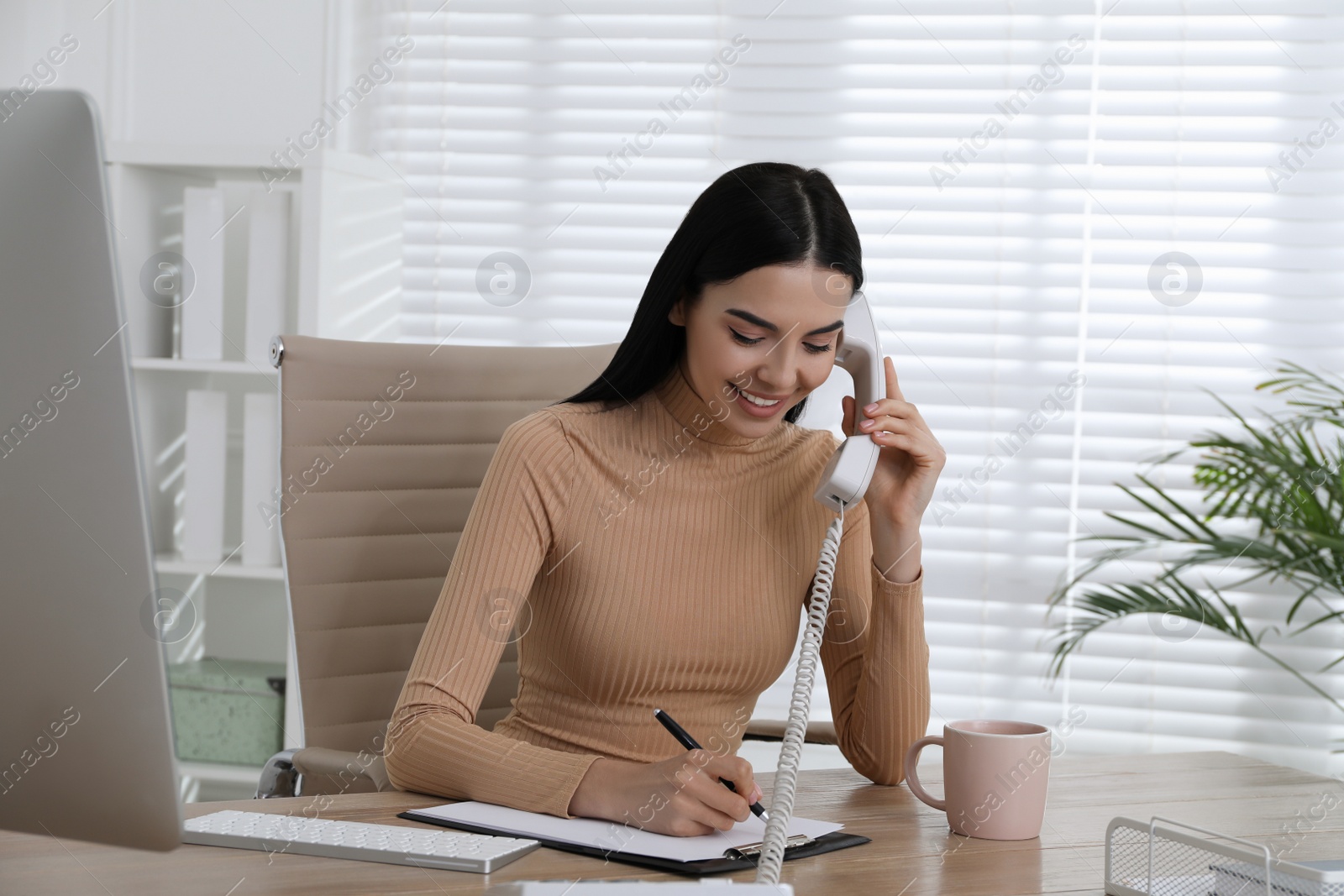 Photo of Secretary talking on phone at wooden table in office