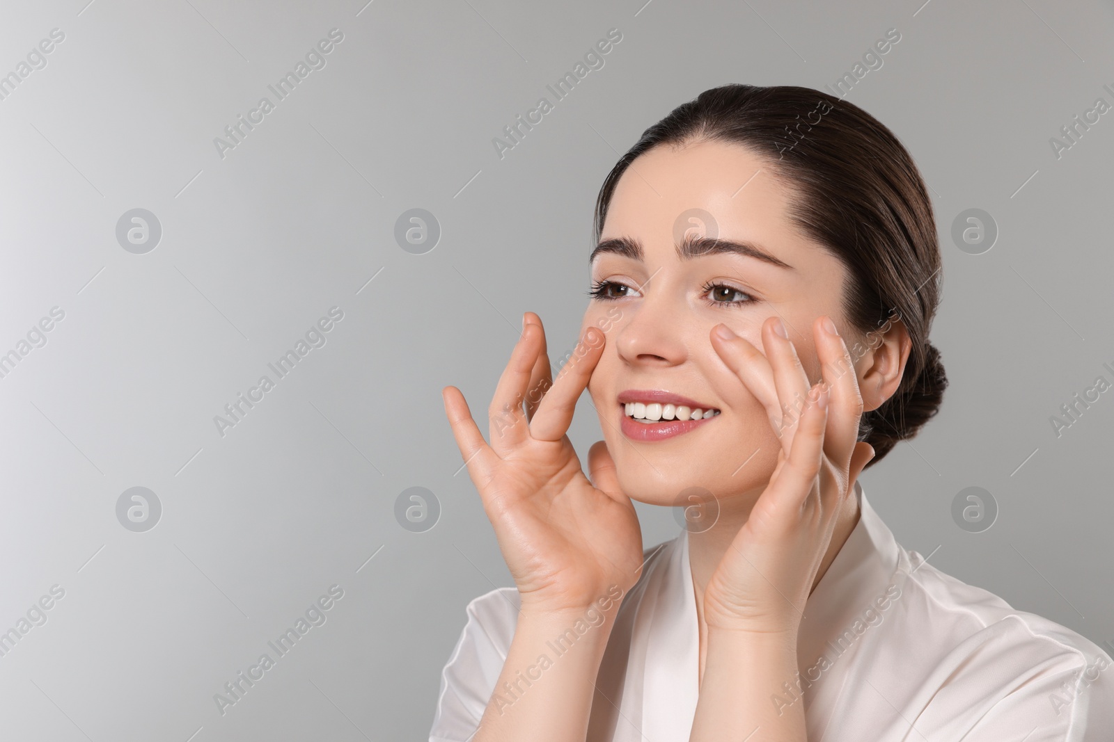 Photo of Young woman massaging her face on grey background. Space for text