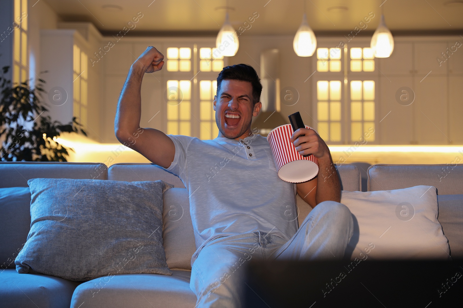 Photo of Man watching movie with popcorn on sofa at night