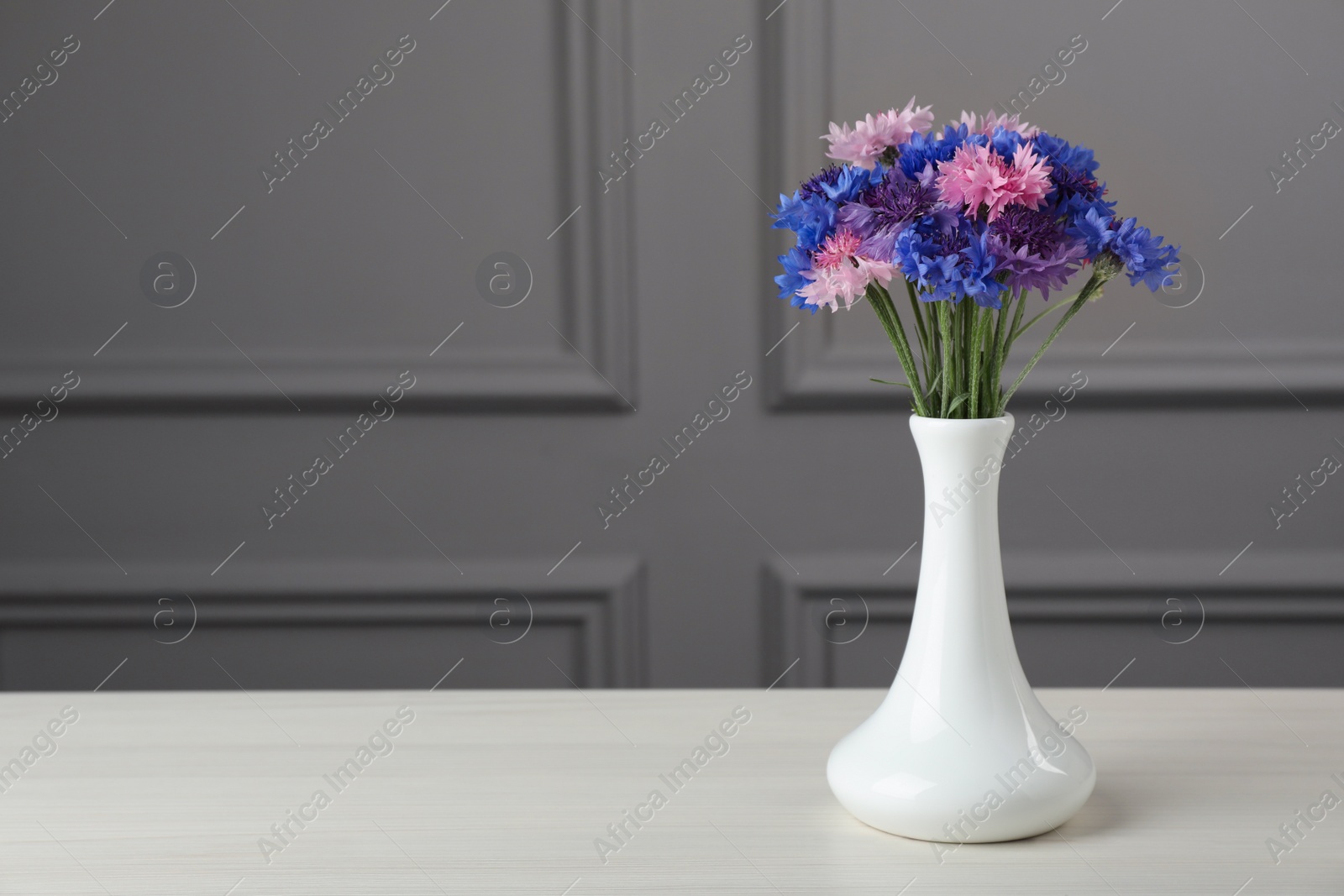 Photo of Bouquet of beautiful cornflowers in vase on white wooden table. Space for text