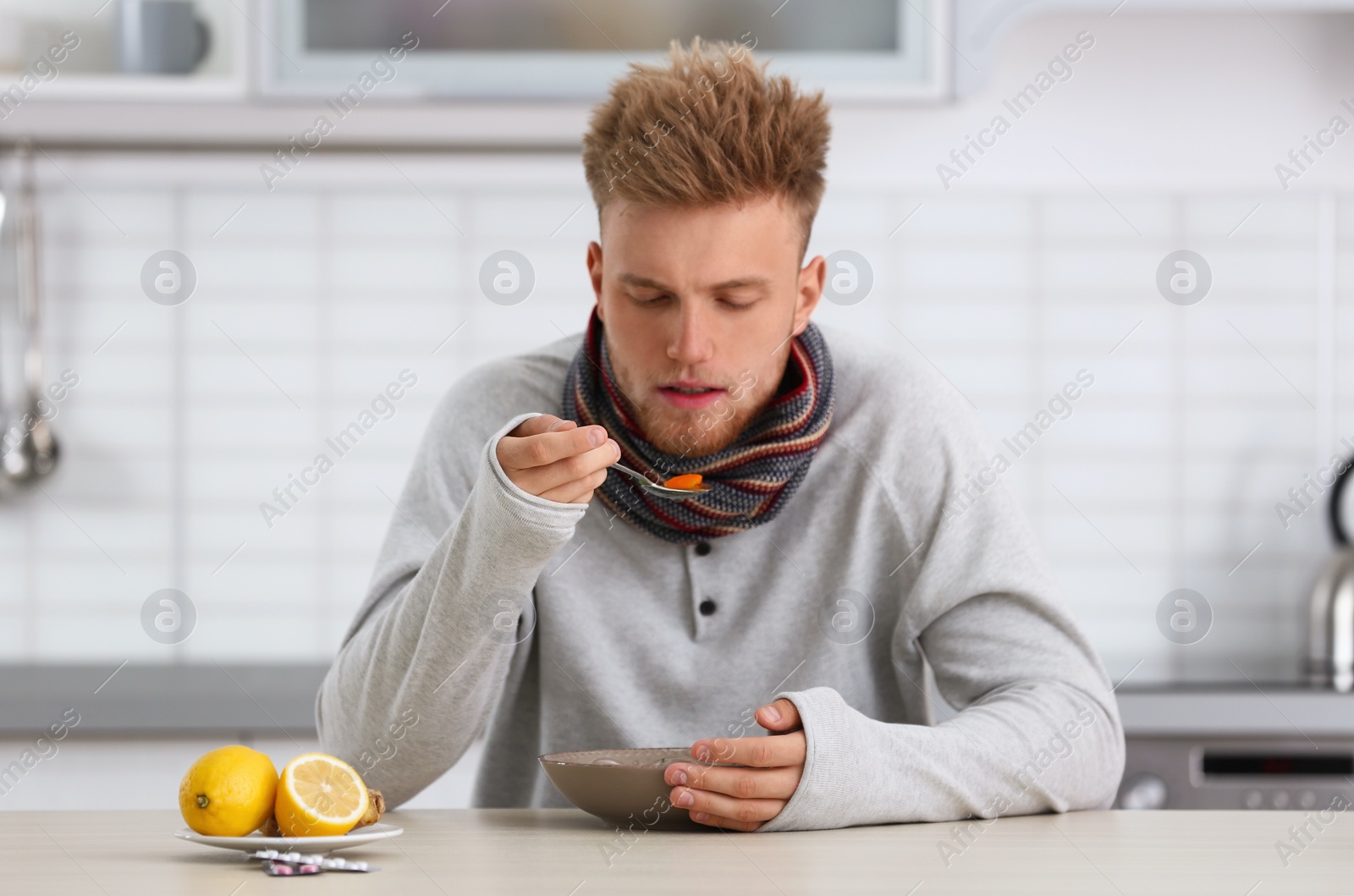 Photo of Sick young man eating soup to cure flu at table in kitchen