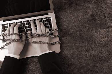 Top view of internet addicted woman with chained hands using laptop at grey table, space for text. Sepia effect