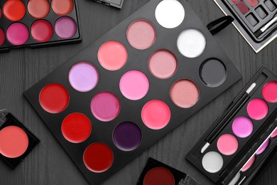 Colorful lipstick palettes on black wooden table, flat lay. Professional cosmetics