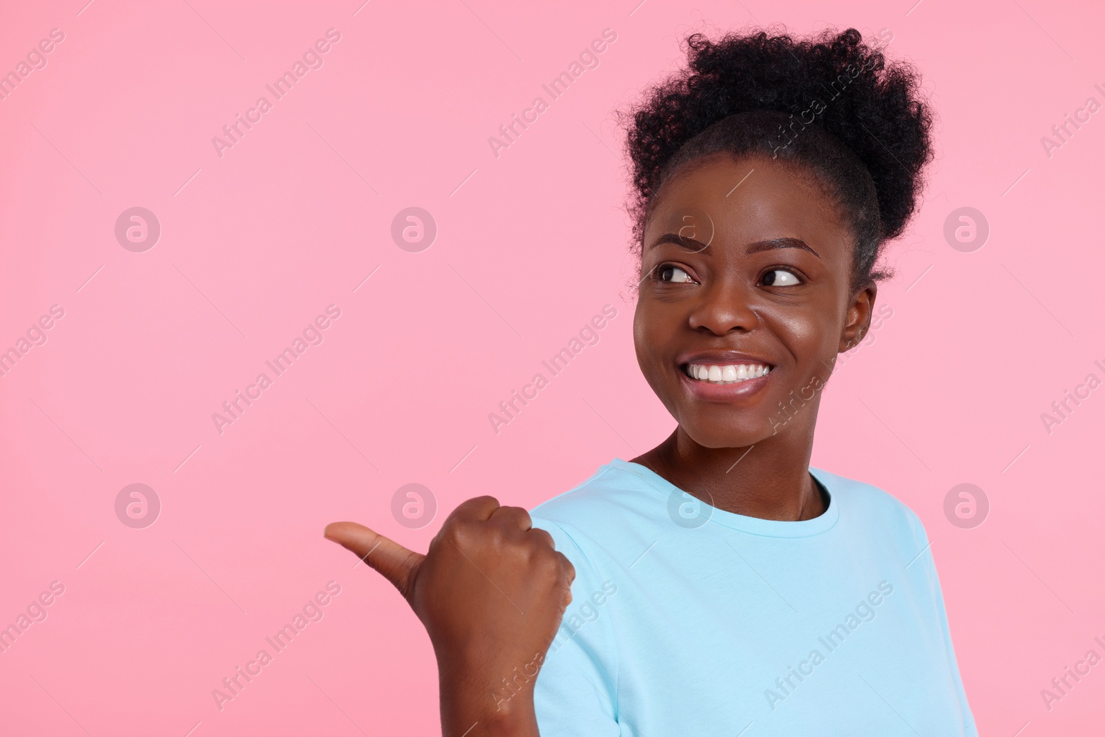 Photo of Happy young woman pointing at something on pink background. Space for text