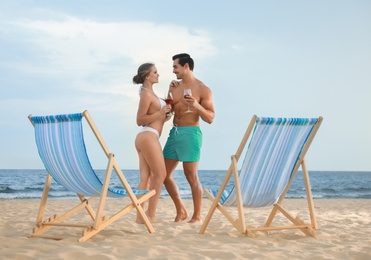 Happy young couple near deck chairs at sea beach