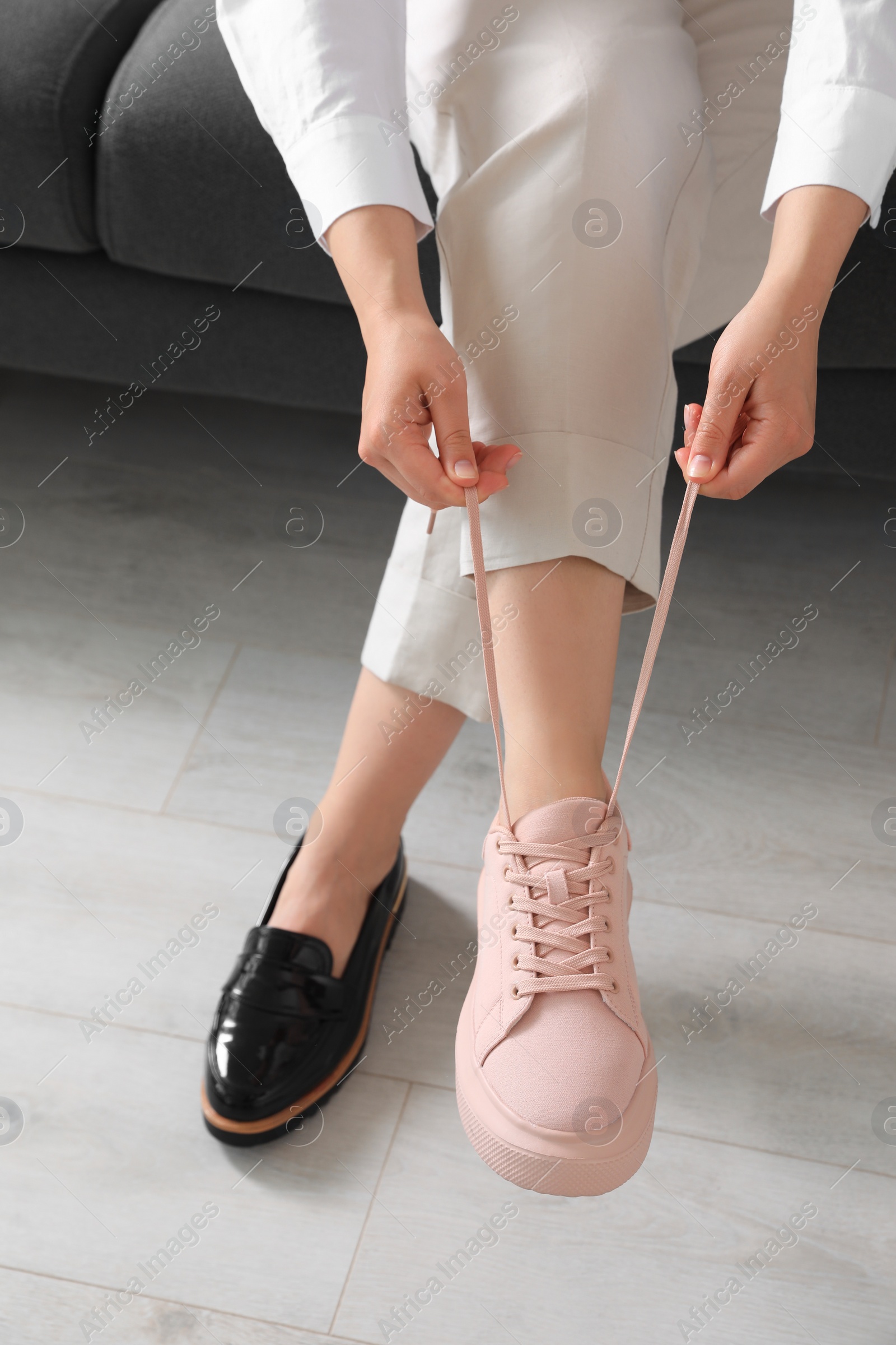 Photo of Woman taking off uncomfortable shoes and putting on sneakers in office, closeup