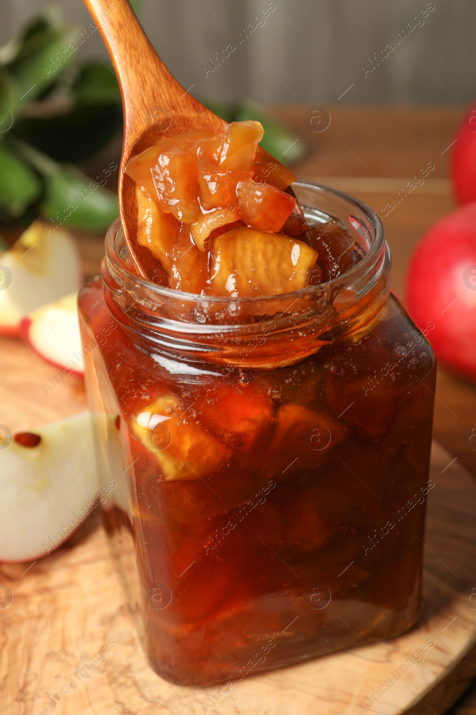 Photo of Spoon with tasty apple jam in glass jar on wooden board, closeup