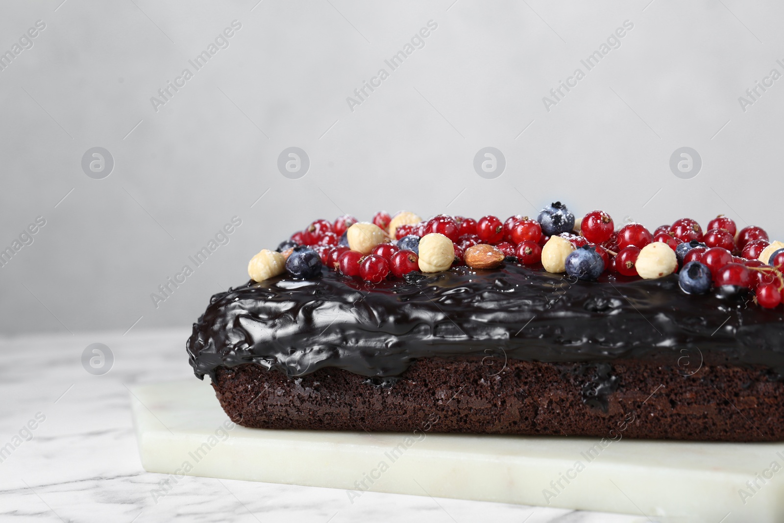 Photo of Delicious chocolate sponge cake with berries and nuts on white marble table, closeup