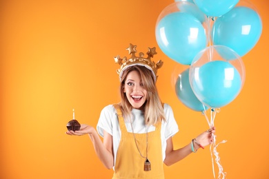 Photo of Young woman with birthday muffin and air balloons on color background