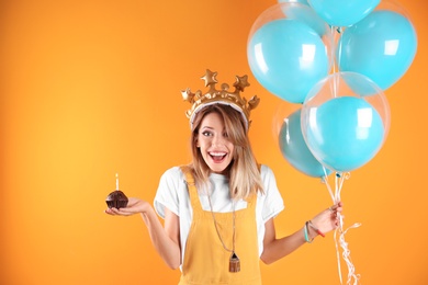 Young woman with birthday muffin and air balloons on color background