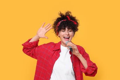 Beautiful young woman with microphone singing on yellow background