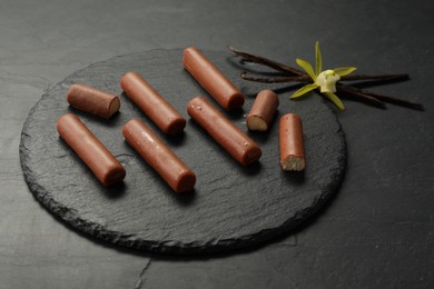 Photo of Glazed curd cheese bars, vanilla pods and flower on black table