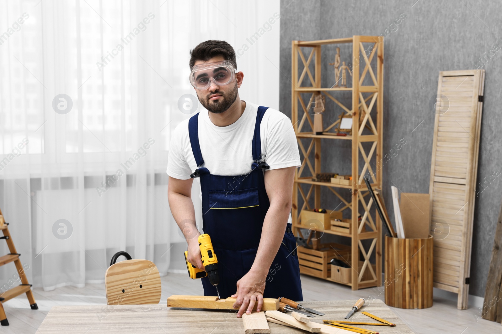 Photo of Young worker using electric drill at table in workshop