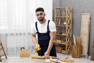 Photo of Young worker using electric drill at table in workshop