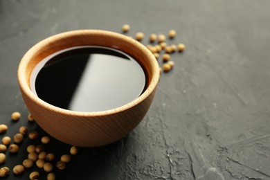 Photo of Tasty soy sauce in bowl and soybeans on black table, closeup. Space for text