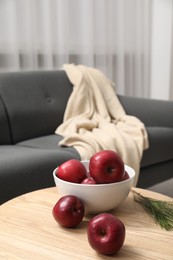 Photo of Red apples on wooden coffee table near grey sofa in room