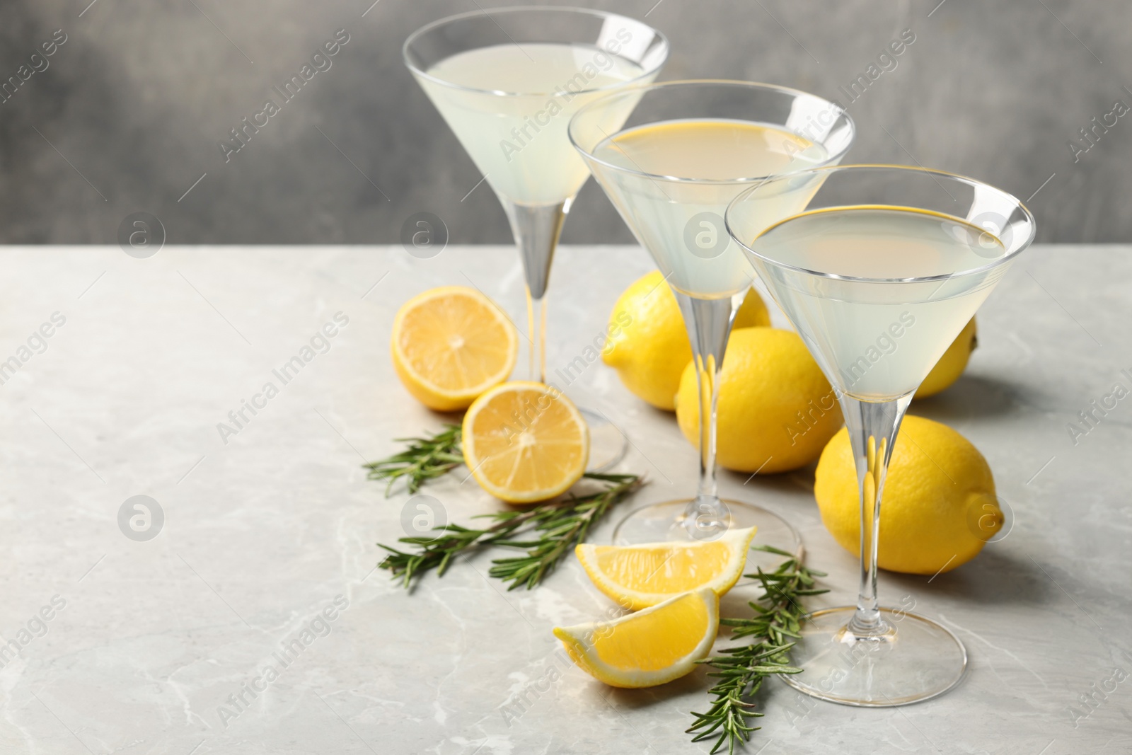 Photo of Martini glasses of refreshing cocktail, lemon and rosemary on light grey textured table. Space for text