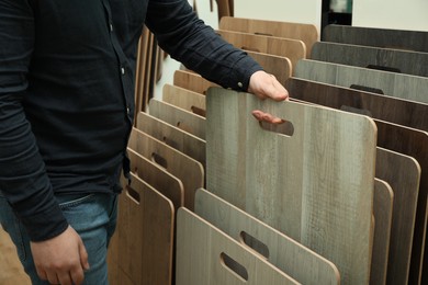 Photo of Man choosing wooden flooring among different samples in shop, closeup