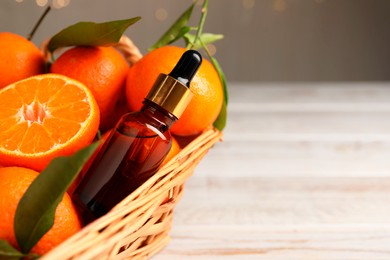 Bottle of tangerine essential oil and fresh fruits in basket, closeup. Space for text