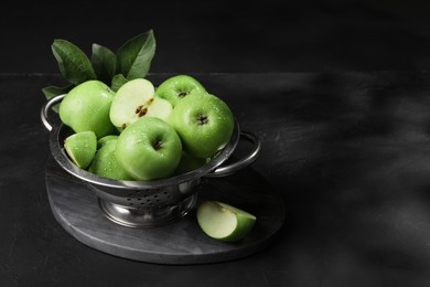 Photo of Ripe green apples with water drops and leaves on black table, space for text