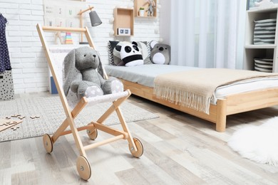 Toy baby buggy with bunny near floor bed indoors. Montessori bedroom interior