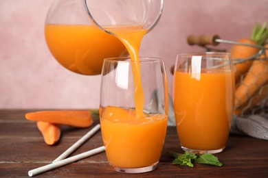 Photo of Pouring freshly made carrot juice into glass on wooden table