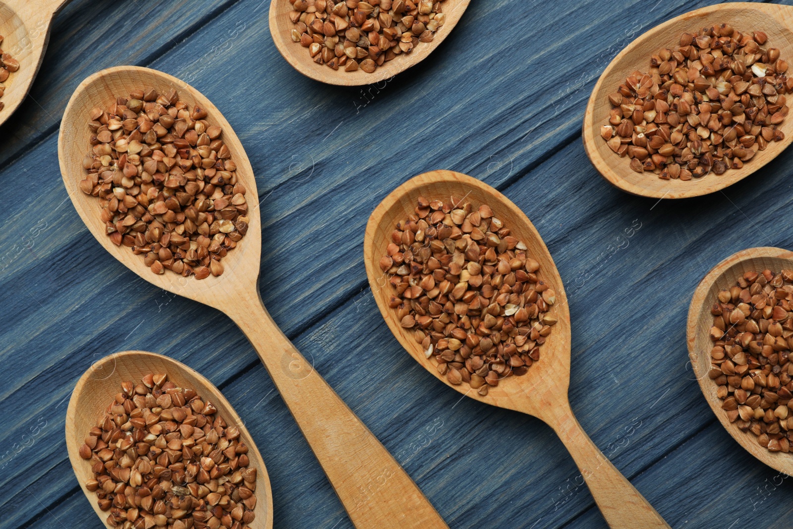 Photo of Buckwheat grains in spoons on blue wooden table, flat lay