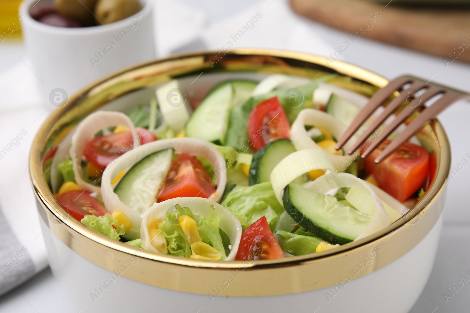 Photo of Bowl of tasty salad with leek, tomatoes and cucumbers on white table, closeup