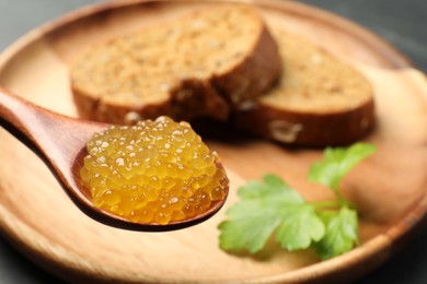 Photo of Fresh pike caviar in spoon, bread and parsley on table, closeup