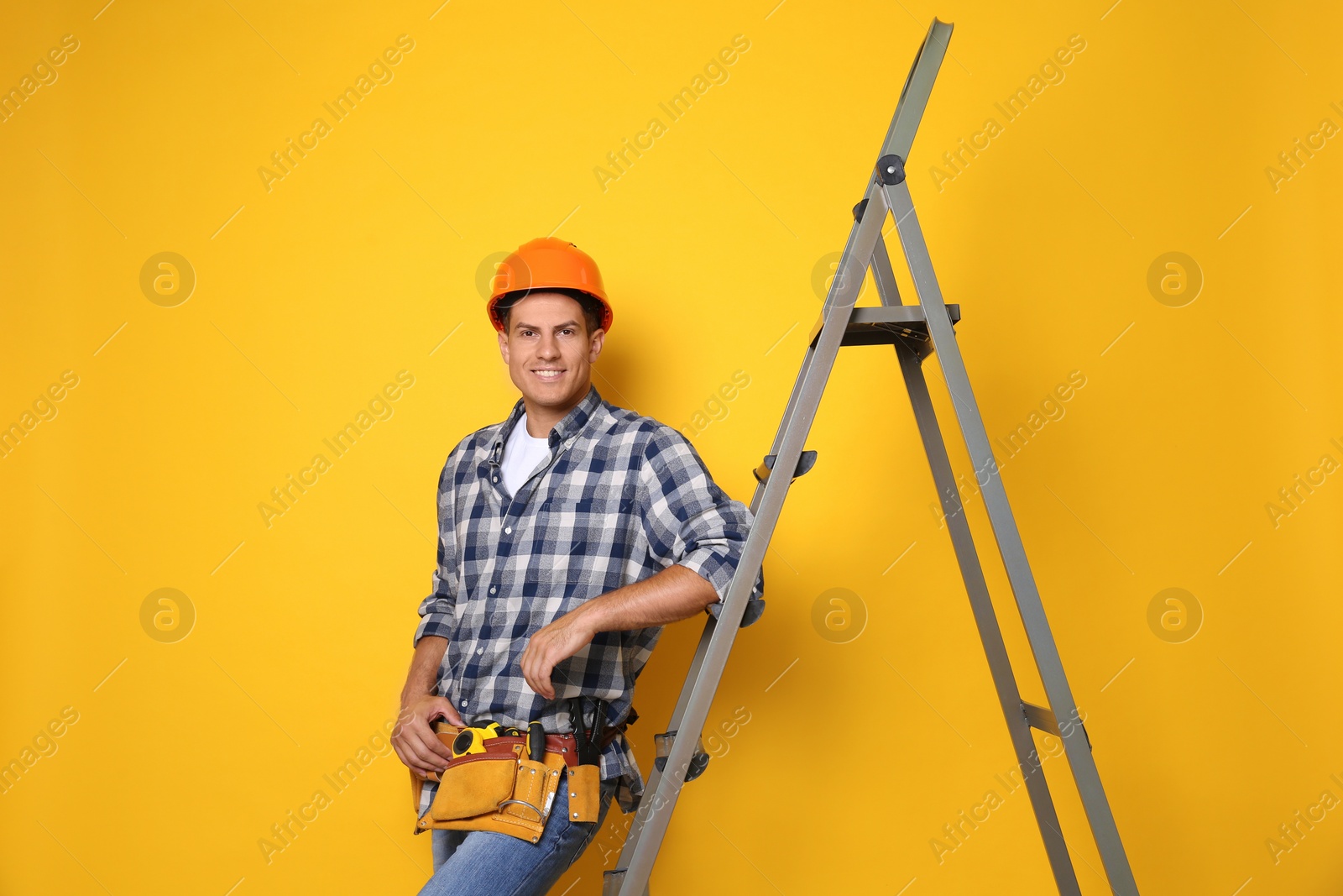 Photo of Professional builder near metal ladder on yellow background