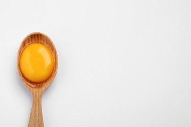 Wooden spoon with raw egg yolk on white 
background, top view. Space for text