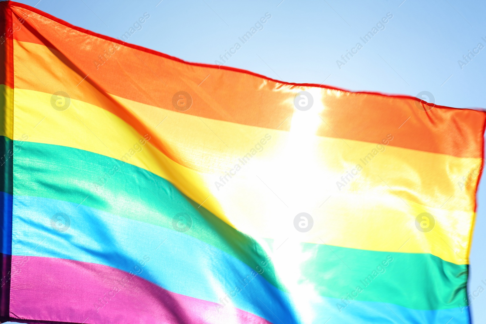Photo of Rainbow LGBT flag fluttering on blue sky background. Gay rights movement