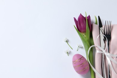 Photo of Cutlery set, Easter egg and tulip on white background, top view with space for text. Festive table setting