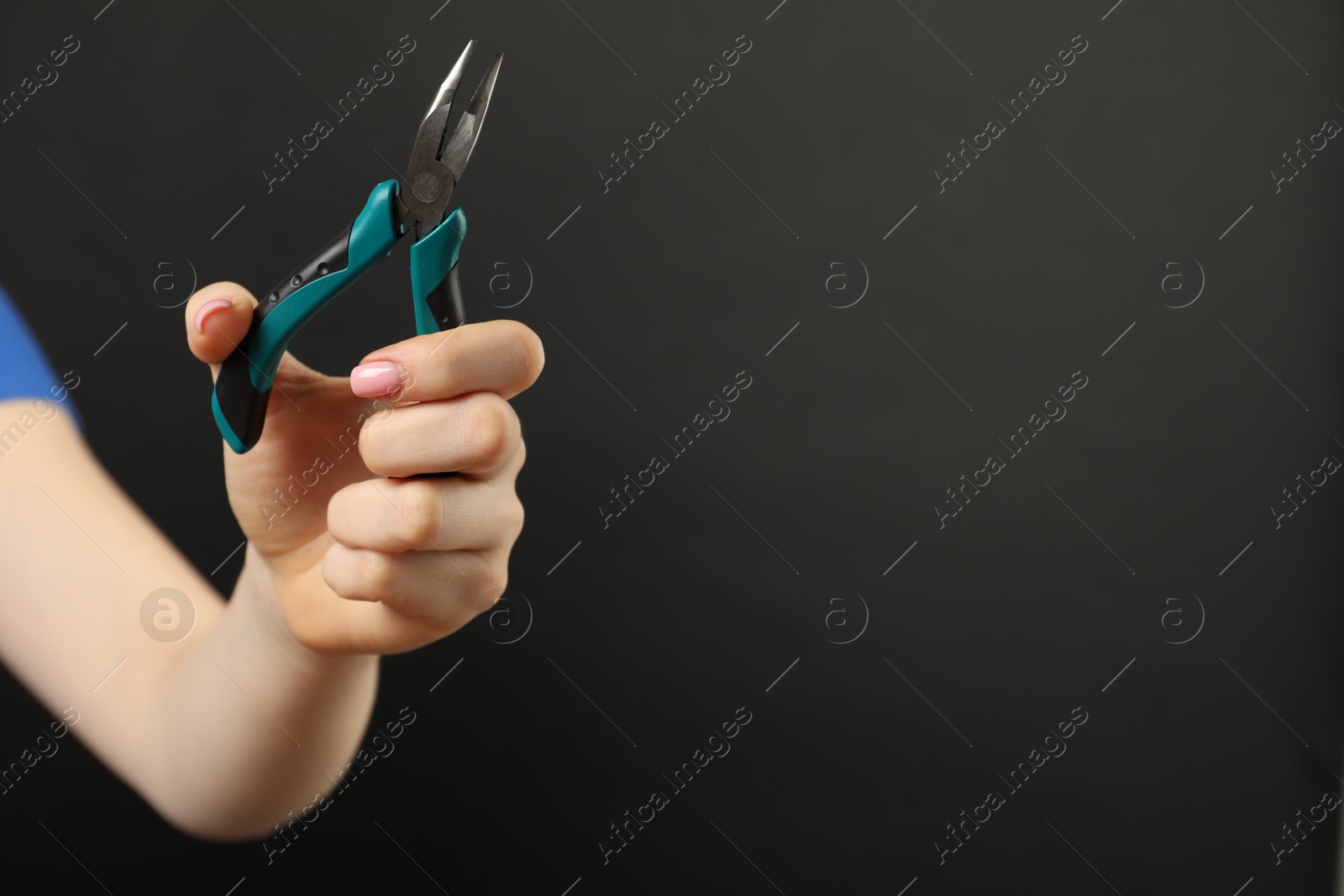 Photo of Woman with bent nose pliers on dark background, closeup. Space for text