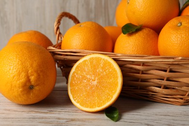 Photo of Many whole and cut oranges on light wooden table, closeup