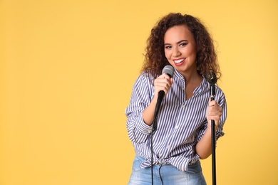 Portrait of curly African-American woman singing in microphone on color background. Space for text