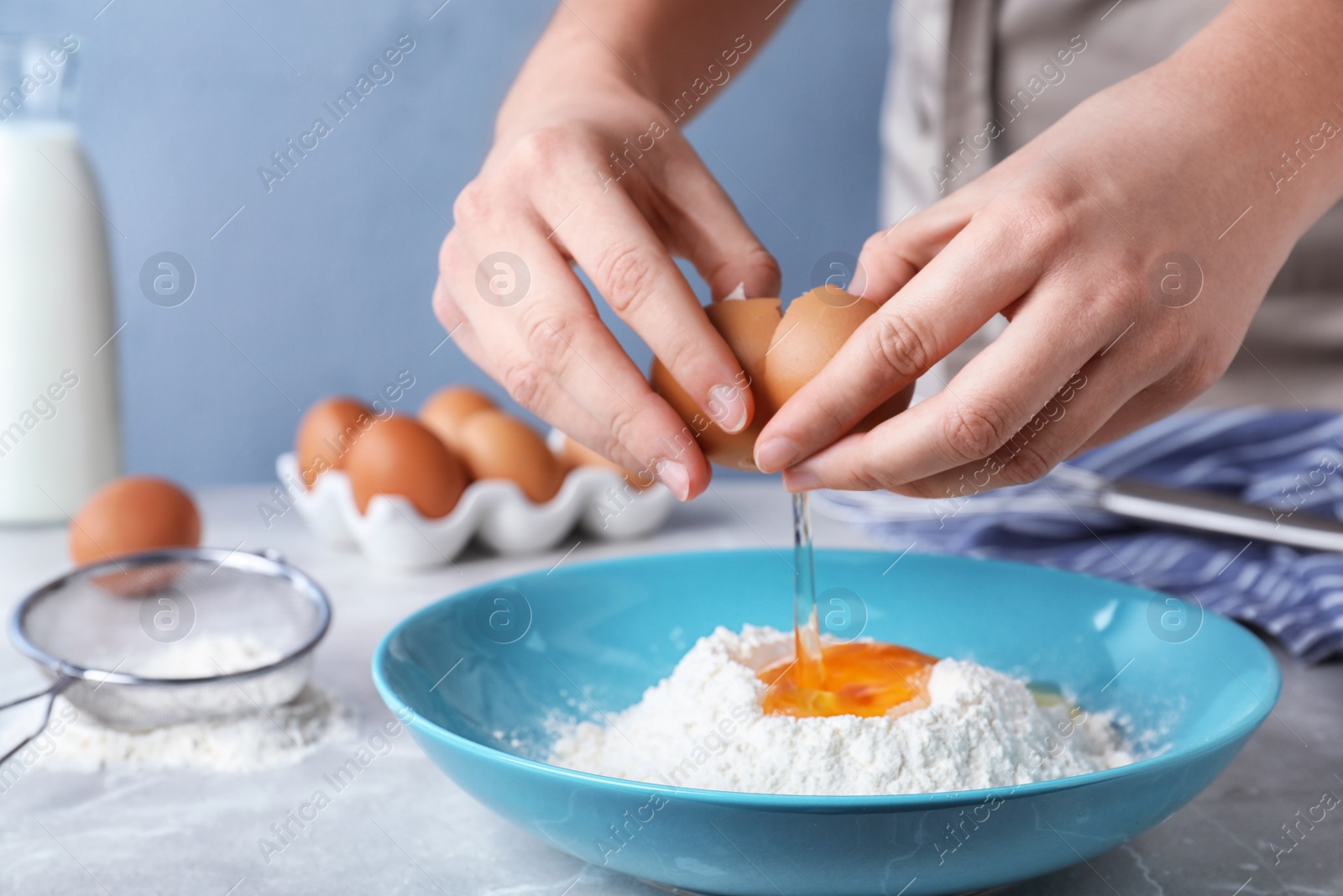 Photo of Woman preparing batter for thin pancakes at light grey table, closeup