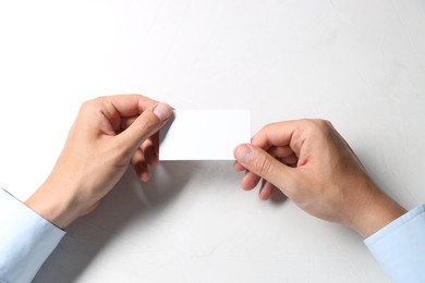 Photo of Man holding blank card at white table, top view. Mockup for design