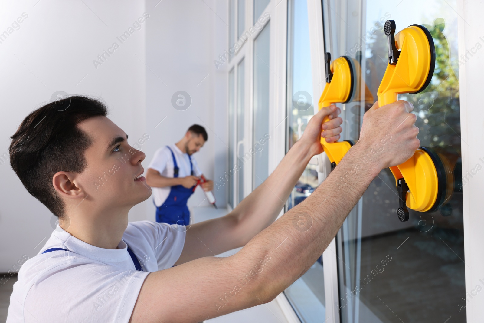 Photo of Worker using suction lifters during plastic window installation indoors