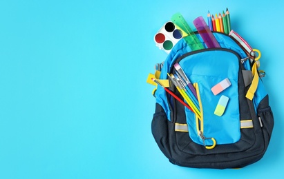 Photo of Stylish backpack with different school stationery on light blue background, top view and space for text. Back to school