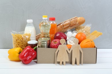 Humanitarian aid for elderly people. Different donation food products and figures of senior couple on white wooden table