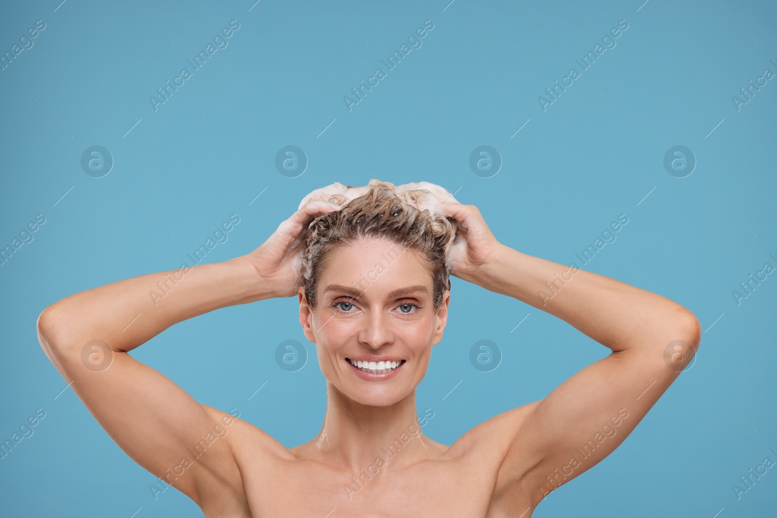 Photo of Beautiful happy woman washing hair on light blue background. Space for text
