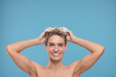 Beautiful happy woman washing hair on light blue background. Space for text