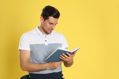 Photo of Handsome man reading book on color background, space for text